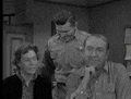 a black and white photo of a group of men standing around a table .