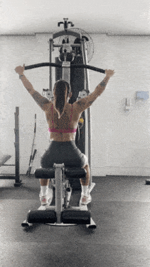 a woman in a pink top is using a machine in a gym