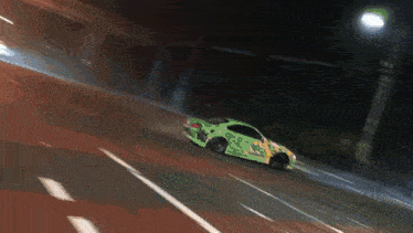 a green sports car is driving down a road at night
