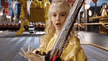 a blonde woman in a yellow dress is holding a large sword .