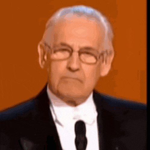 a man wearing glasses and a suit and tie looks at the camera