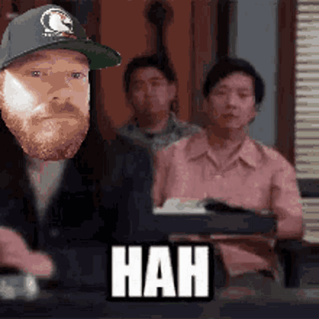 a man with a beard wearing a hat is sitting in front of a sign that says " hah "