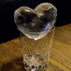 a heart shaped ice cube in a glass of water on a table .
