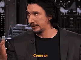 a man in a suit is making a funny face and saying `` come in '' while talking to someone .