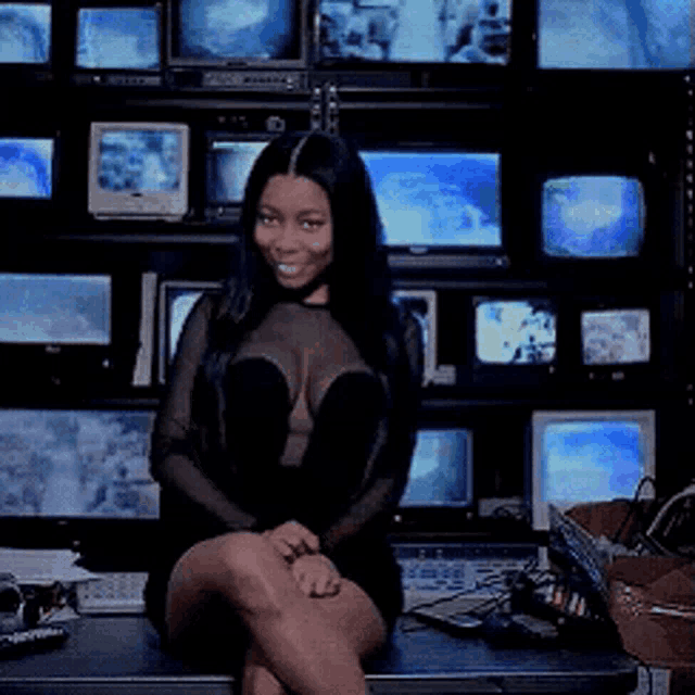 a woman sitting in front of a wall of televisions