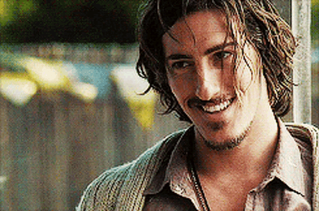 a man with long hair and a beard smiles for the camera