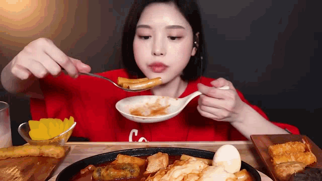 a woman in a red shirt is eating food from a plate with a spoon .