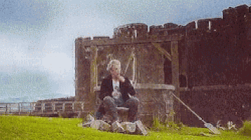a man is sitting on a rock in front of a castle smoking a cigarette .