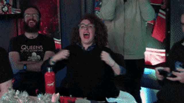 a woman wearing a queens shirt is laughing in front of a group of people