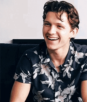 a man wearing a floral shirt is smiling and sitting on a couch