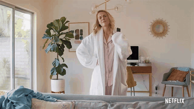 a woman in a bathrobe is standing in a living room with a netflix logo on the corner