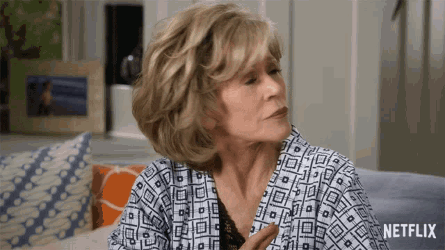 an older woman is sitting on a couch with a netflix logo behind her