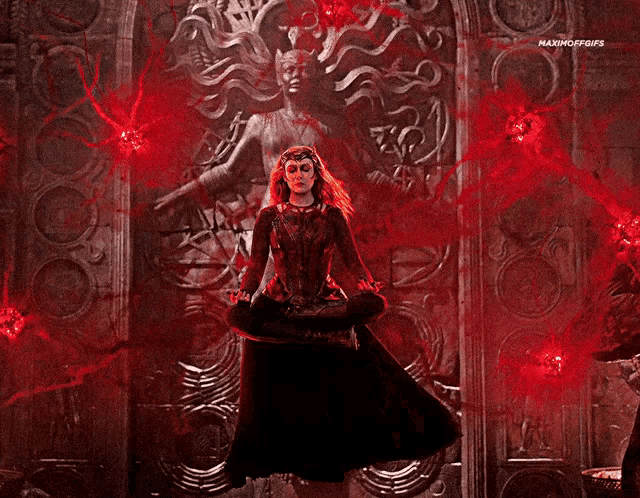 scarlet witch is sitting in a lotus position in front of a statue surrounded by red glowing lights .