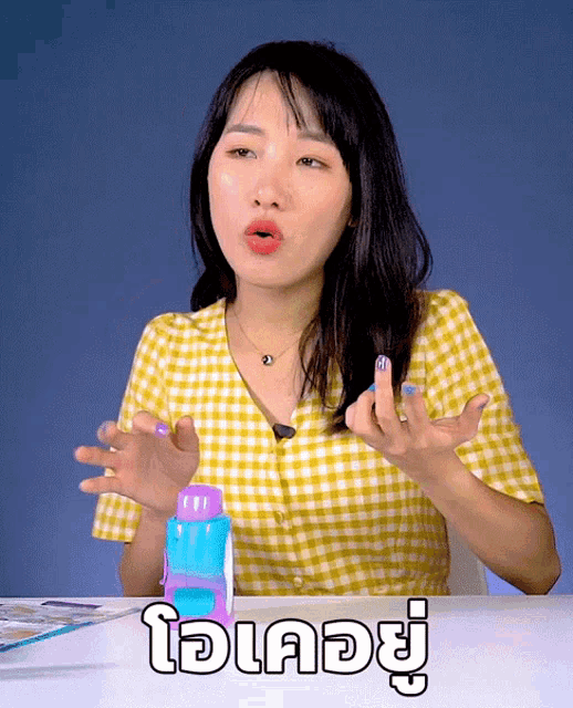 a woman in a yellow plaid shirt is sitting at a table in front of a sign that says ' oi '