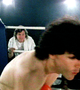 a man in a white shirt is standing in a boxing ring with another man