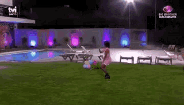 a person is playing with balloons on a lush green lawn in front of a swimming pool .