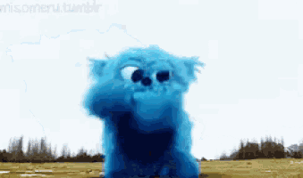 a blue stuffed animal is standing in the middle of a field ..