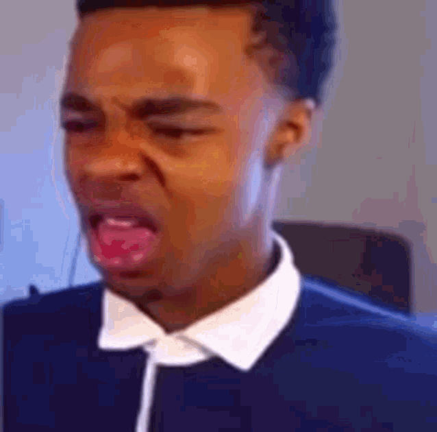 a man in a blue shirt and white collar is making a funny face .