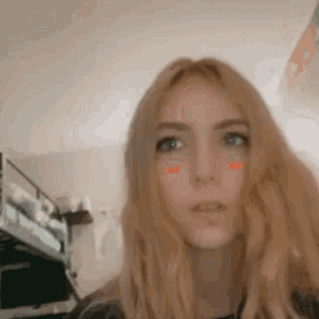 a woman with long blonde hair is making a funny face in a bedroom .