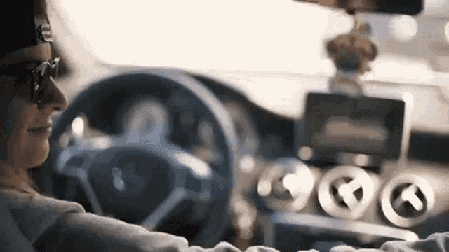 a man is driving a car with a hat on and sunglasses on