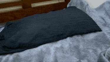 a black pillow is laying on a gray blanket on a bed