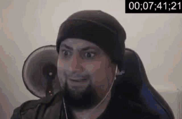 a man with a beard is sitting in a chair wearing headphones and a hat .