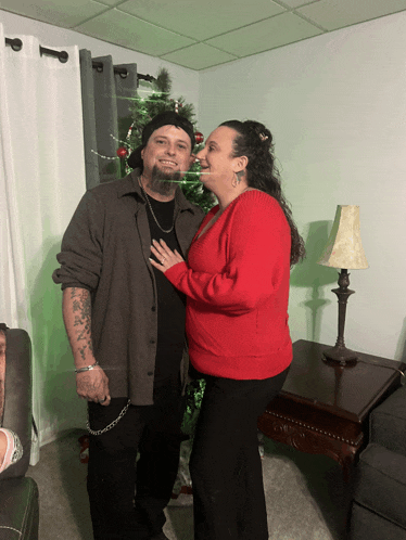 a man and a woman pose for a picture in front of a christmas tree
