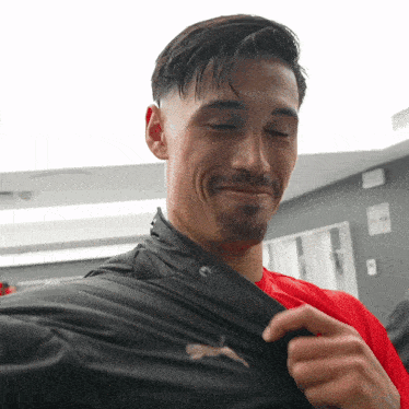 a man wearing a red shirt and a black jacket with the word puma on it