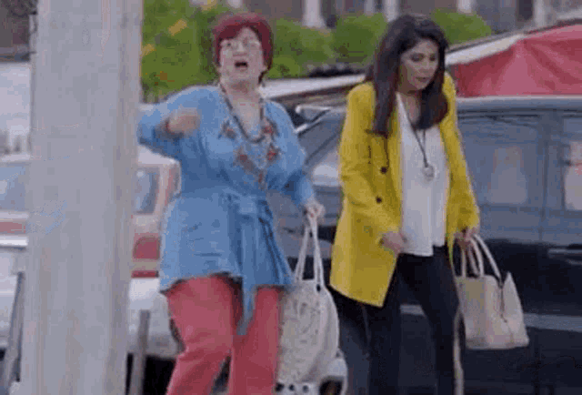 two women are standing next to each other on a street holding handbags .