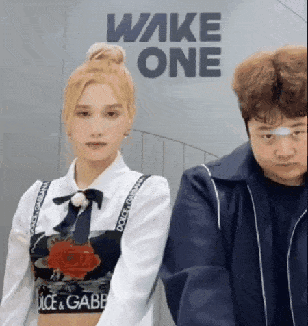 a man and a woman are standing next to each other in front of a wall with the word wake one on it .