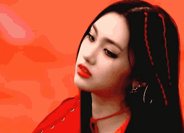 a woman with long black hair and red lips is wearing a red top