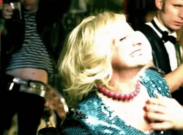 a woman in a blue sequined dress with a pink necklace is dancing