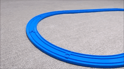 a toy train is going around a blue track on a carpeted floor