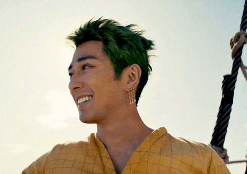 a man with green hair is smiling and wearing earrings