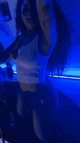 a woman in a white tank top is dancing in a dark room with blue lights .
