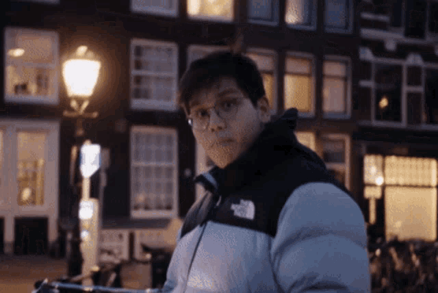 a man wearing a north face jacket stands in front of a street light