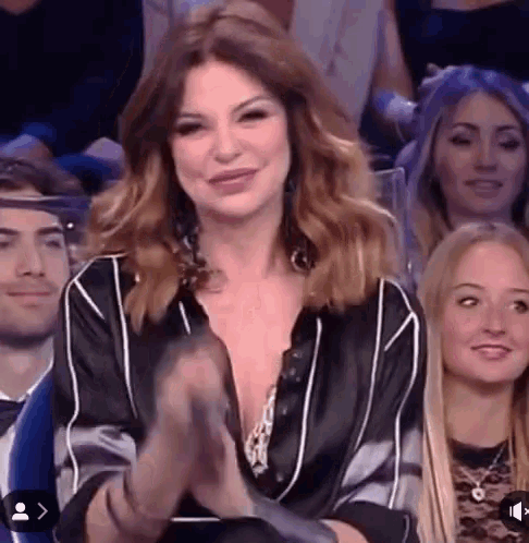 a woman is sitting in a crowd clapping her hands and smiling .
