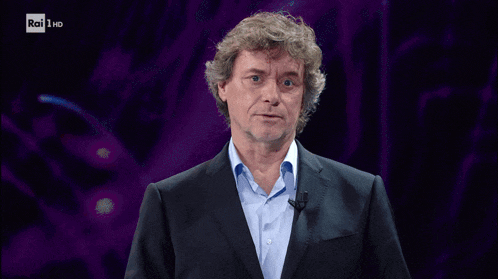 a man in a suit stands in front of a rai 1 hd screen