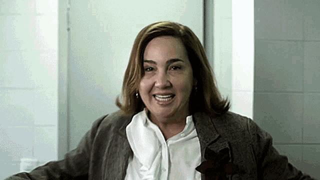 a woman wearing a brown jacket and a white shirt smiles