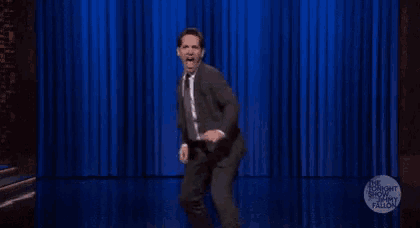 a man in a suit and tie is dancing on stage in front of a blue curtain .