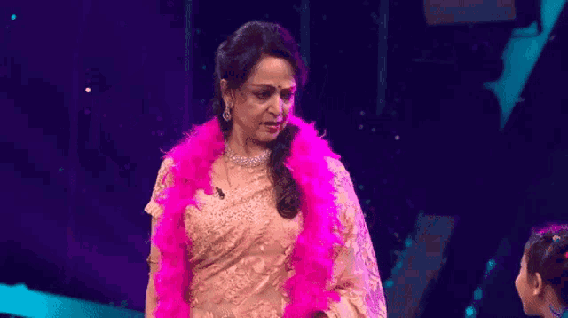 a woman is wearing a pink boa around her neck and standing on a stage .