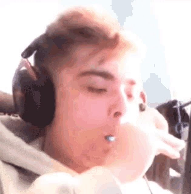 a young man wearing headphones is blowing a bubble with a microphone in his mouth .