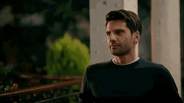 a man in a black sweater is standing on a porch looking at the camera .