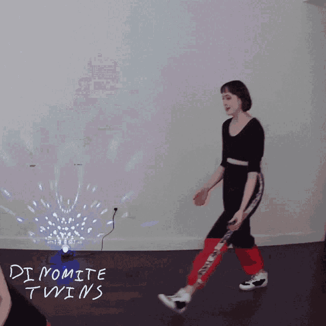 a woman is dancing in front of a wall that says dynamite twins on it