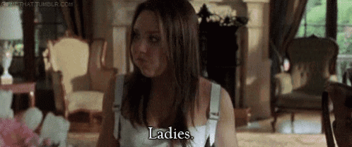 a woman in a white tank top is sitting in a living room talking to a man .