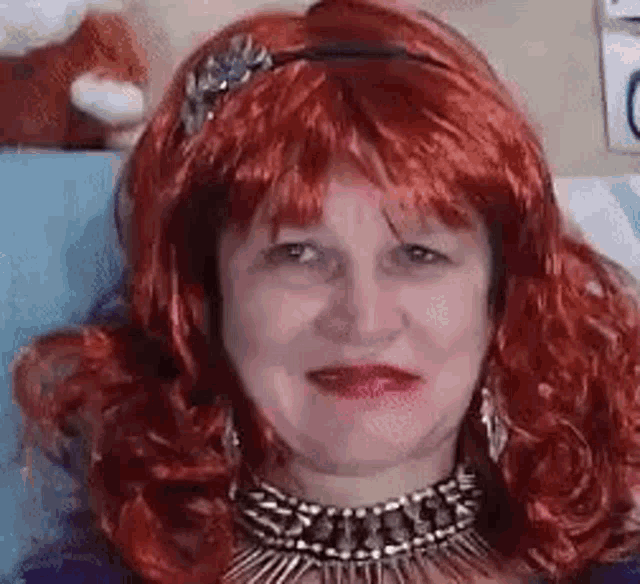 a woman wearing a red wig and a gold necklace is smiling .