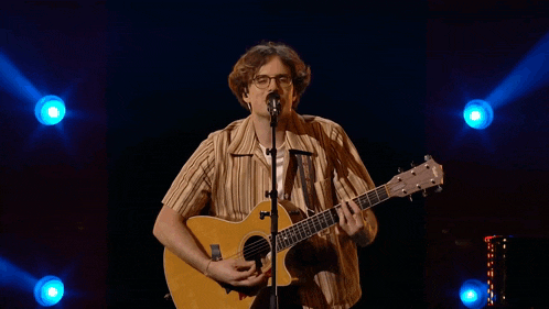 a man is singing into a microphone while holding a guitar