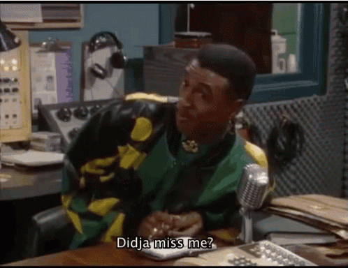 a man in a green and yellow jacket is sitting at a desk with a microphone and says didja miss me ?