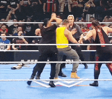 a man in a yellow tank top stands in a wrestling ring with two other men