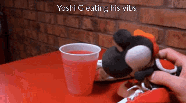 yoshi g is eating his yibs next to a cup of liquid